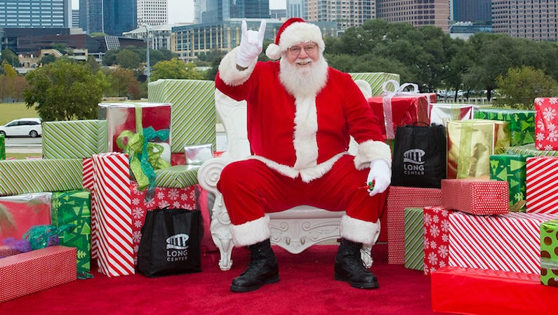 Santa holding up Texas symbol with hands for the Santa on the Terrace event for Top Holiday Kids Events This Weekend in Austin. 